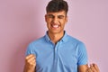 Young indian man wearing blue polo standing over isolated pink background very happy and excited doing winner gesture with arms Royalty Free Stock Photo