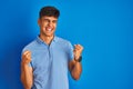 Young indian man wearing casual polo standing over isolated blue background very happy and excited doing winner gesture with arms Royalty Free Stock Photo