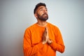 Young indian man wearing orange sweater over isolated white background begging and praying with hands together with hope