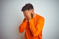 Young indian man wearing orange sweater over isolated white background with sad expression covering face with hands while crying Royalty Free Stock Photo