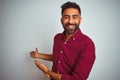 Young indian man wearing red elegant shirt standing over isolated grey background Inviting to enter smiling natural with open hand