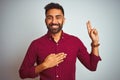 Young indian man wearing red elegant shirt standing over isolated grey background smiling swearing with hand on chest and fingers Royalty Free Stock Photo
