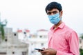 Young Indian man wearing surgical mask and showing smartphone to camera. Royalty Free Stock Photo