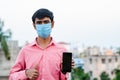 Young Indian man wearing surgical mask and showing smartphone to camera. Royalty Free Stock Photo