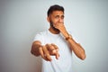 Young indian man wearing t-shirt standing over isolated white background laughing at you, pointing finger to the camera with hand Royalty Free Stock Photo