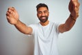 Young indian man wearing t-shirt standing over isolated white background looking at the camera smiling with open arms for hug Royalty Free Stock Photo