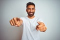 Young indian man wearing t-shirt standing over isolated white background pointing to you and the camera with fingers, smiling Royalty Free Stock Photo