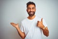 Young indian man wearing t-shirt standing over isolated white background Showing palm hand and doing ok gesture with thumbs up, Royalty Free Stock Photo