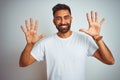 Young indian man wearing t-shirt standing over isolated white background showing and pointing up with fingers number ten while Royalty Free Stock Photo