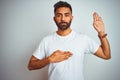 Young indian man wearing t-shirt standing over isolated white background Swearing with hand on chest and open palm, making a