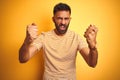 Young indian man wearing t-shirt standing over isolated yellow background angry and mad raising fists frustrated and furious while