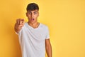 Young indian man wearing white t-shirt standing over isolated yellow background pointing displeased and frustrated to the camera, Royalty Free Stock Photo
