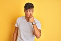 Young indian man wearing white t-shirt standing over isolated yellow background Pointing to the eye watching you gesture, Royalty Free Stock Photo