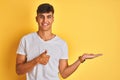 Young indian man wearing white t-shirt standing over isolated yellow background Showing palm hand and doing ok gesture with thumbs Royalty Free Stock Photo