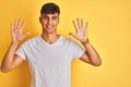Young indian man wearing white t-shirt standing over isolated yellow background showing and pointing up with fingers number ten Royalty Free Stock Photo