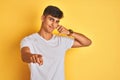 Young indian man wearing white t-shirt standing over isolated yellow background smiling doing talking on the telephone gesture and Royalty Free Stock Photo