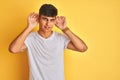 Young indian man wearing white t-shirt standing over isolated yellow background Trying to hear both hands on ear gesture, curious