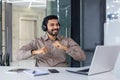 A young Indian man works in the office. He sits at his desk with headphones in front of his laptop and dances during the Royalty Free Stock Photo