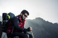 Young indian mountaineer sitting on the top of the mountain on a cliff with a backpack and a stick, enjoying the view from the top Royalty Free Stock Photo