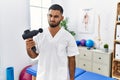 Young indian physiotherapist holding therapy massage gun at wellness center skeptic and nervous, frowning upset because of problem Royalty Free Stock Photo