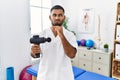 Young indian physiotherapist holding therapy massage gun at wellness center thinking worried about a question, concerned and Royalty Free Stock Photo