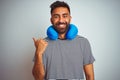 Young indian tourist man on travel wearing neckpillow over isolated white background smiling with happy face looking and pointing Royalty Free Stock Photo