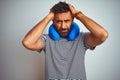 Young indian tourist man on travel wearing neckpillow over isolated white background suffering from headache desperate and