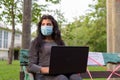 Young Indian woman with mask thinking and using laptop while sitting with distance on park bench Royalty Free Stock Photo