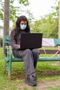 Young Indian woman with mask using laptop while sitting with distance on park bench Royalty Free Stock Photo