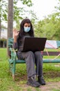 Young Indian woman with mask video calling while sitting with distance on park bench Royalty Free Stock Photo