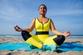 Young indian woman practice asanas on blue yogic mat on goa beach . she wearing stylish yellow leggings and fitness top