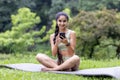 Indian woman practicing yoga and using smartphone in park ambiance Royalty Free Stock Photo