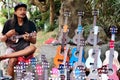 Young Indonesian vendor playing the guitar in his souvenirs street shop in JL Monkey Forest road, Ubud.