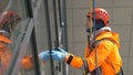 Industrial climber in orange overalls and helmet washes windows on tall building outside. Royalty Free Stock Photo