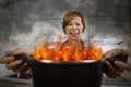 Young inexperienced home cook woman in panic with apron holding pot burning in flames with in panic Royalty Free Stock Photo