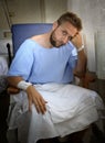 Young injured man in hospital room sitting alone in pain worried for his health condition