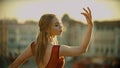 A young inspired woman in red dress standing on the roof and gracefully posing for the camera - bright sunset