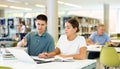 Young interested couple of students spending time together in library, reading books and browsing educational websites Royalty Free Stock Photo