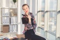 Young interior designer sitting on a work table smiling, looking at camera, holding sketchbook and ruler. Front view