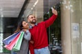 Young international couple with bright paper bags taking selfie near big shopping centre, copy space Royalty Free Stock Photo