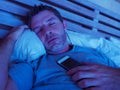 Young internet addict man sleeping on bed holding mobile phone in his hand at night in smartphone and social media network overuse Royalty Free Stock Photo