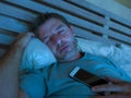 Young internet addict man sleeping on bed holding mobile phone in his hand at night in smartphone and social media network overuse Royalty Free Stock Photo