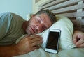 Young internet addict man sleeping on bed holding mobile phone in his hand in smartphone and social media overuse and online addic Royalty Free Stock Photo