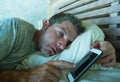 Young internet addict man sleeping on home couch holding mobile phone in his hand in smartphone and social media overuse and onlin