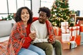 Young interracial couple drinking coffee sitting on the sofa by christmas tree at home Royalty Free Stock Photo