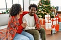 Young interracial couple drinking coffee sitting on the sofa by christmas tree at home Royalty Free Stock Photo