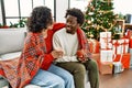 Young interracial couple drinking coffee sitting on the sofa by christmas tree at home Royalty Free Stock Photo