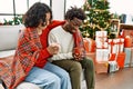 Young interracial couple drinking coffee sitting on the sofa by christmas tree at home Royalty Free Stock Photo