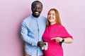 Young interracial couple expecting a baby holding shoes smiling happy pointing with hand and finger Royalty Free Stock Photo