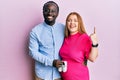 Young interracial couple expecting a baby holding shoes smiling with an idea or question pointing finger with happy face, number Royalty Free Stock Photo